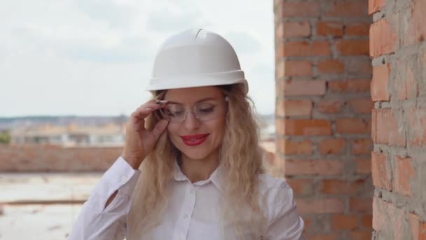 Female architect in business attire and a white helmet stands at the construction site — Stok video