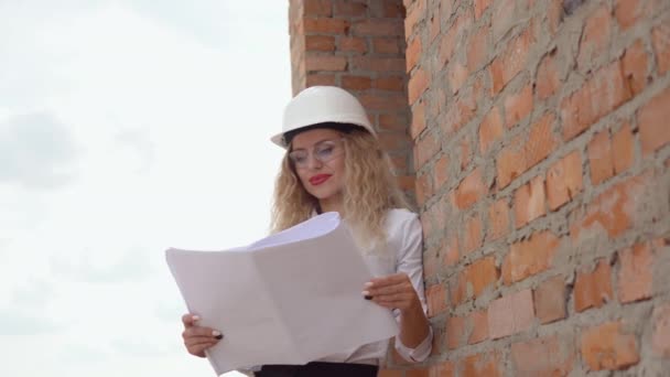 Female architect in business attire standing outdoors at construction site. The architect reads the architectural plan — Stock Video