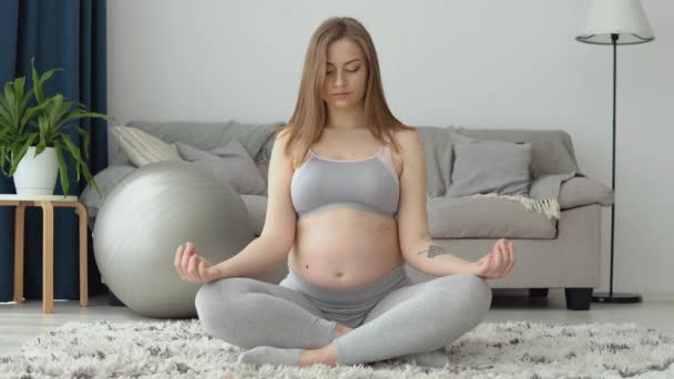 Mulher grávida em sportswear sentado no tapete na posição de lótus. Cuidados de saúde na gravidez. Yoga para mulheres grávidas — Vídeo de Stock
