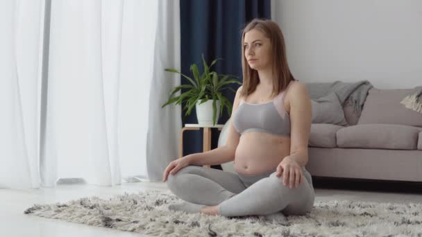 Zwangere vrouw in sportkleding zittend op het tapijt in de lotuspositie. Gezondheidszorg tijdens de zwangerschap. Yoga voor zwangere vrouwen — Stockvideo