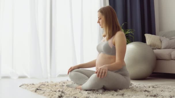 Terhes nő sportruházatban ül a szőnyegen lótuszpozícióban. Egészségügyi ellátás a terhesség alatt. Jóga terhes nők számára — Stock videók
