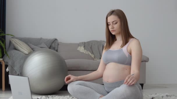 Zwangere vrouw in sportkleding zittend op het tapijt in de lotuspositie. Gezondheidszorg tijdens de zwangerschap. Yoga voor zwangere vrouwen — Stockvideo