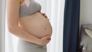 Hamile bir kadın ellerini karnına koyar. Hamilelik sırasında esneme izi olmayan sağlıklı nemlendirilmiş deri. Hamile kadınlar için cilt bakımı. Karnındaki gerilme izlerinin önlenmesi.