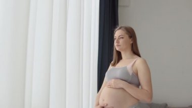 Güzel hamile kadın pencerenin yanında duruyor. Bebek bekliyorum.