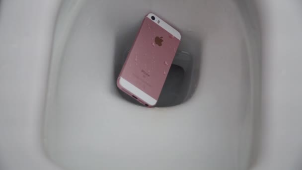 2021年7月1日:ピンクと白のiPhoneが水で白いトイレに落ちます。水との接触によるスマートフォンの故障。携帯電話は修理できません。 — ストック動画