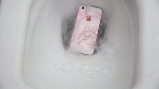 Нью-Йорк, США - 1 ИЮЛЯ 2021 года: Розовый и белый iPhone падает в белый туалет с водой. Сбой смартфона из-за контакта с водой. Вода в туалете капает — стоковое видео