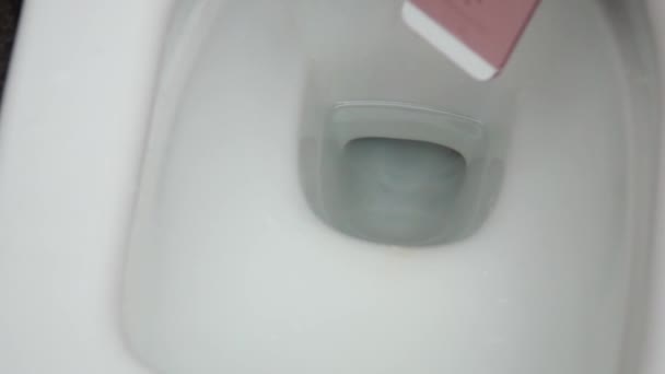 New York, USA - JULI 1, 2021: Roze en witte iPhone valt in een wit toilet met water. Storing van de smartphone door contact met water. De mobiele telefoon kan niet worden gerepareerd — Stockvideo