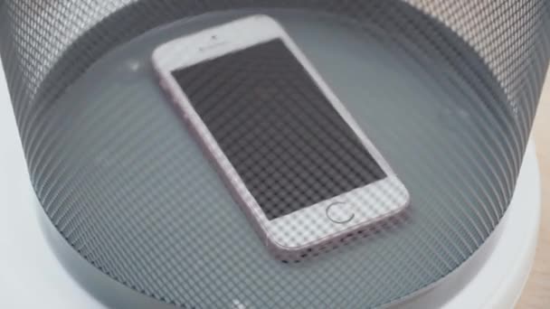 New York, États-Unis - 1er juillet 2021 : Un vieux smartphone blanc et rose défectueux se trouve au fond de la poubelle. La poubelle tourne. Vue latérale à travers le réseau de poubelles. Réparation de téléphone portable — Video