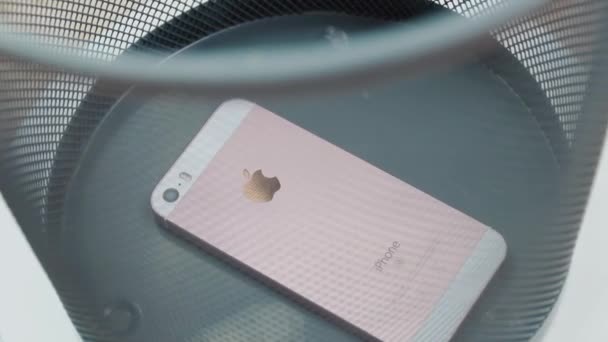 New York, USA - 1 LUGLIO 2021: Un vecchio iPhone bianco e rosa difettoso si trova in fondo alla spazzatura. Il bidone della spazzatura gira. Vista laterale attraverso il cestino reticolo. Riparazione cellulare — Video Stock