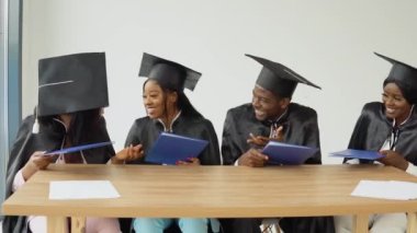 Afrika kökenli dört üniversite ya da üniversite mezunu ellerinde diplomalarla oturup birbirleriyle konuşarak eğleniyorlar.