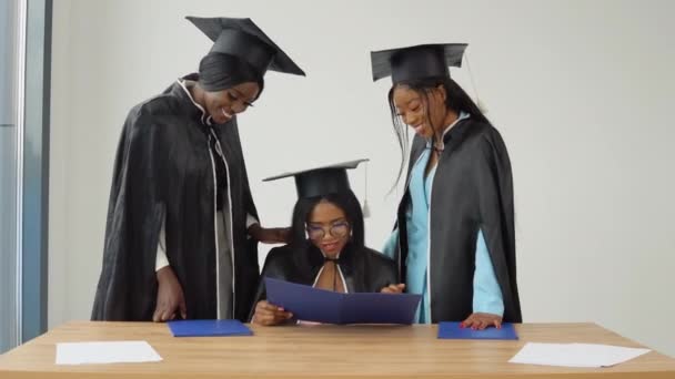 Une femme est assise à un bureau, et deux camarades de classe se tiennent derrière elle, regardant les notes de fin d'études. — Video