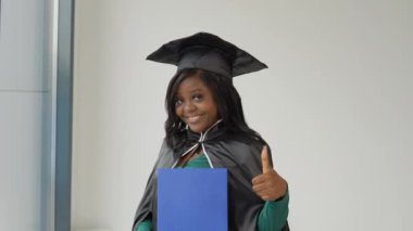 Klasik üstat kıyafeti ve manto giymiş Afrika kökenli bir bayan mezun elinde diplomayla ve gülümseyerek ayakta duruyor. Tıp Fakültesi 'nin sevgili mezunuyum. Yurtdışındaki kadınlar için yüksek öğrenim