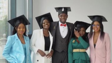 Genç, neşeli bir genç adam ve dört mutlu kız üniversite mezunları usta şapkalarıyla kameranın önünde dikiliyorlar. Samimi gülümseme