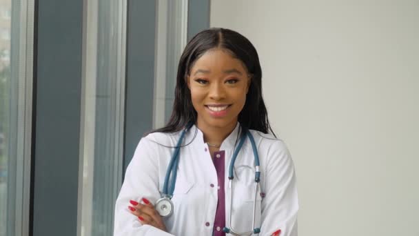 Una joven mujer afroamericana graduada con un vestido médico blanco sonríe y posa para la cámara. Un evento importante. Especialista joven — Vídeos de Stock