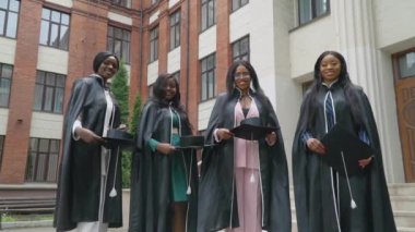 Geleneksel usta şapkası fırlatma. Şapkalar kameraya doğru uçar. Klasik takım elbiseli ve siyah cüppeli dört mezun eski bir Avrupa üniversitesinin tuğla cephelerinin yanında duruyor.