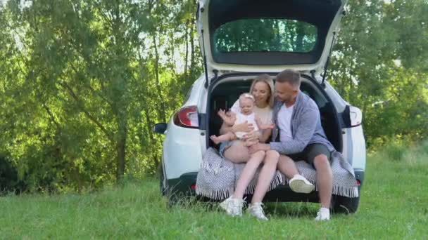 Traditionelle Familie mit einem kleinen Mädchen, das außerhalb der Stadt im Kofferraum eines Autos ruht. Kaukasische junge Vater und Mutter spielen mit ihrer Tochter — Stockvideo