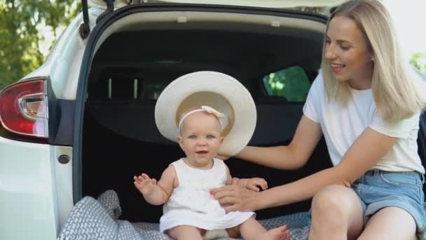 Gelukkige moeder en stijlvolle baby de stad uit. De moeder laat haar dochter een hoed zien en helpt haar hem te passen. Witte gezinsauto. — Stockvideo