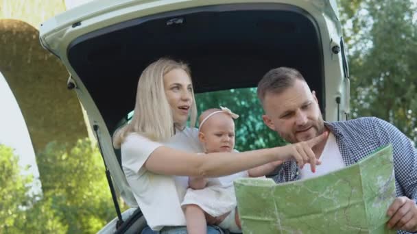 Šťastná rodina cestuje autem. Otec a matka drží holčičku v náručí a dívají se na cestovní mapu. Aktivní volný čas pro rodinu — Stock video