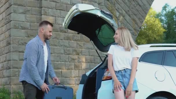 Happy couple travels by car. Man and woman fold suitcases to the trunk of a car. Active leisure for young people — Stock Video