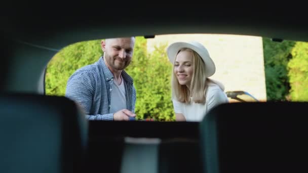 คู่รักที่มีความสุขเดินทางโดยรถยนต์ ผู้ชายและผู้หญิงพับกระเป๋าเดินทางไปที่ท้ายรถ พักผ่อนหย่อนใจสําหรับคนหนุ่มสาว มุมมองจากท้ายรถ — วีดีโอสต็อก