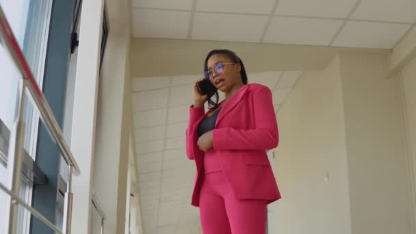 Czarująca afrykańska biznesmenka w różowym garniturze rozmawiająca przez komórkę w biurze — Wideo stockowe