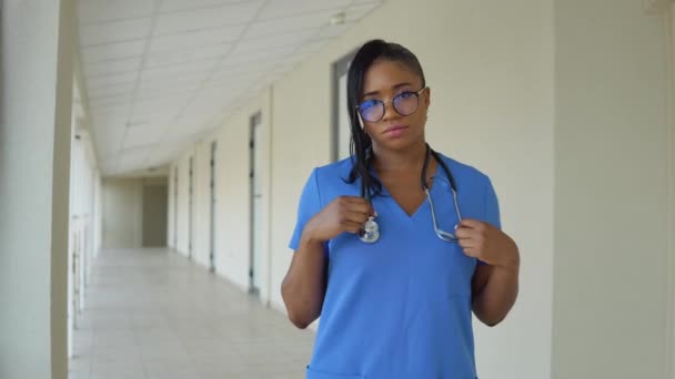 Eine junge afroamerikanische Ärztin im blauen Anzug steht im Flur der Klinik und untersucht eine Röntgenaufnahme der Brust eines Erwachsenen. — Stockvideo