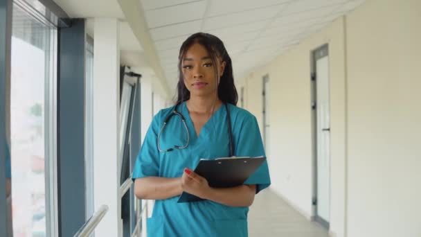 Una giovane dottoressa afroamericana vestita di blu si trova nel corridoio della clinica ed esamina i documenti — Video Stock