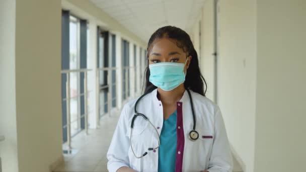 Jonge Afro-Amerikaanse arts vrouw in een blauw pak en witte jas draagt een wegwerp steriel gezicht masker — Stockvideo