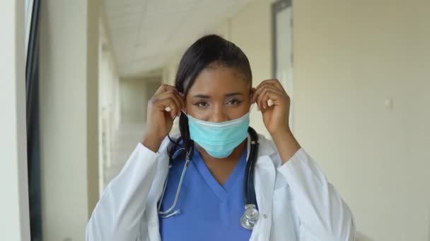 Νεαρή Αφροαμερικανή γιατρός με μπλε κοστούμι και λευκό παλτό αφαιρεί αποστειρωμένη μάσκα προσώπου μιας χρήσης — Αρχείο Βίντεο