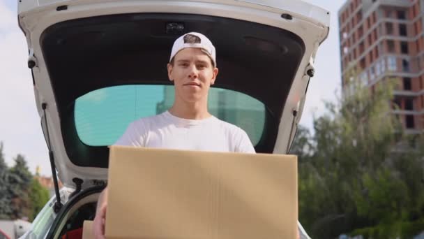 Üretilmiş malların taşınması ve teslimatı. Bir çalışan elinde bir kutu tutar ve paketlerle dolu bir arabanın yanında durur. — Stok video