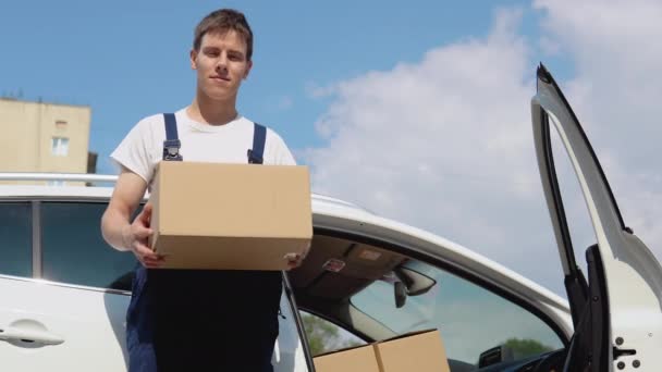 Üretilmiş malların taşınması ve teslimatı. Sürücü kargo belgelerini doldurur ve kameraya bakar. Bir çalışan elinde bir kutu tutar ve paketlerle dolu bir arabanın yanında durur. — Stok video