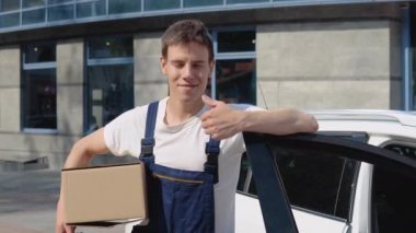 Üretilmiş malların taşınması ve teslimatı. Sürücü kargo belgelerini doldurur ve kameraya bakar. Bir çalışan elinde bir kutu tutar ve paketlerle dolu bir arabanın yanında durur.