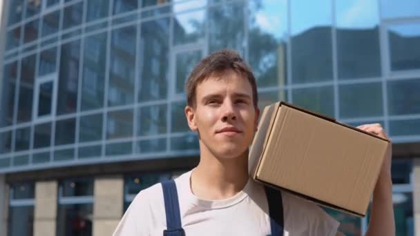 The courier carries a box on his shoulder against the background of a glass modern high-rise building — Stock Video