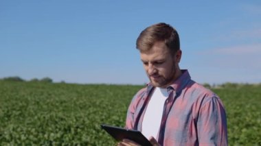 Genç bir çiftçi, tarladaki soya fasulyelerinin özellikleri hakkında bir tablete notlar yazar.