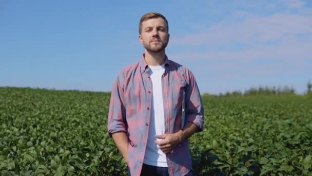 Een jonge boer staat midden in een sojaveld — Stockvideo