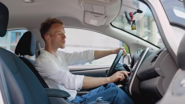 Elegante hombre rizado joven moderno presiona botones en el panel del dispositivo en su coche eléctrico — Vídeo de stock