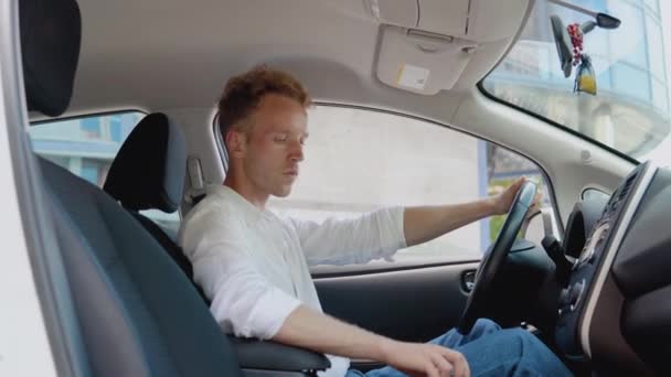 Elegante jovem homem encaracolado moderno inicia seu carro elétrico. Um homem aprende a conduzir um carro — Vídeo de Stock