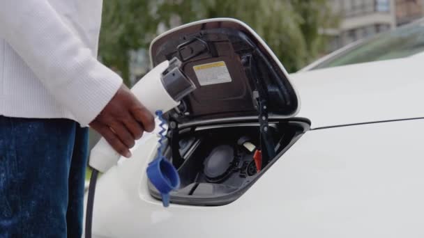 Mladý Afroameričan připojí elektrické auto k nabíječce. Proces napojení elektromobilu na nabíječku. Pohled zblízka — Stock video