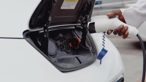 Um jovem afro-americano liga um carro eléctrico ao carregador. O processo de conexão do carro elétrico para o carregador. Vista de perto — Vídeo de Stock
