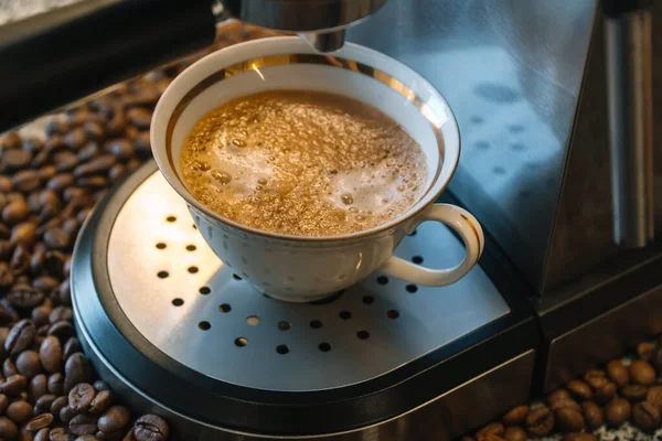 O processo de derramar café de uma máquina de café em uma pequena xícara de porcelana branca com douramento — Fotografia de Stock