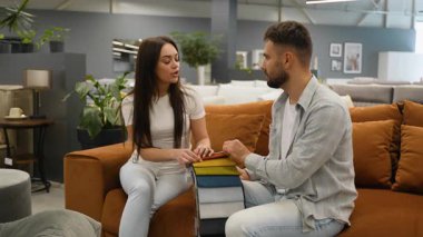 Mobilya galerisindeki yeni bir koltukta oturan mutlu genç çift ve kumaş kumaş rengini bir kitaptan seçerek ev içleri için ortak bir karar veriyorlar.