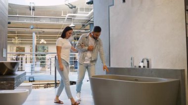 Genç bir çift modern bir banyo malzemesi dükkanına giriyor, lüks bir banyo küvetini dikkatle inceliyor ve evlerini yenilemeyi planlıyorlar ve birlikte önemli bir alışveriş yapıyorlar.