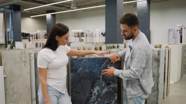 Genç çift yeni ev tasarımları için koyu mermer desenli seramik seramik fayansları tartışıyor ve seçiyor.