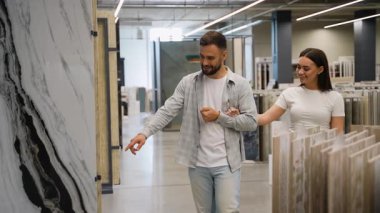 Genç ve mutlu bir çift, yeni evleri için seramik ya da porselen seramik fayanslar seçerek ve ev dekorasyonu için tasarım seçeneklerini tartışarak bir hırdavatçı dükkanında yürüyorlar.