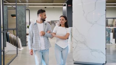 Bir hırdavatçı dükkanında yürüyen mutlu genç çift, yeni ev dekorasyonu ve yenileme projeleri için büyük format seramik veya porselen seramik seramiklerini tartışıyor ve seçiyorlar.