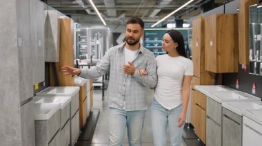 Ev dekorasyonu mağazasında el ele yürürken, yeni banyo lavabolarını, makyaj malzemelerini ve dolaplarını tartışan ve seçen mutlu beyaz çift.