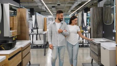 Ev dekorasyonu projesi sırasında yeni mobilya ve hijyenik eşyalar seçerek ev dekorasyonu mağazasında el ele yürüyen mutlu genç çift seçeneklerini tartışıyor.