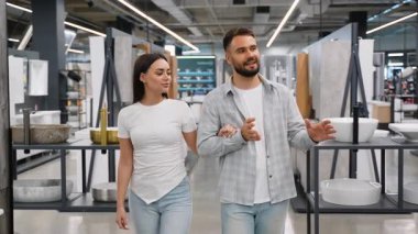Genç çift ev dekorasyonu mağazasında kol kola yürüyor, aktif olarak yeni mobilya ve lavaboları tartışıyor ve seçiyorlar.