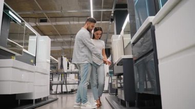 Geniş, modern bir galeride yeni banyo mobilyaları almak için alışverişe çıkan mutlu genç çift, bir gösteriş aletini inceliyor ve yeni evleri ya da daireleri için en iyi seçeneği seçiyor.