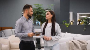 Modern bir galeride genç bir bayan müşteriye profesyonel erkek mobilya danışmanı tavsiye ediyor. Tatmin olmuş müşteri ve başarılı satıcı anlaşmayı sonuçlandırır ve anlaşmaya varır.